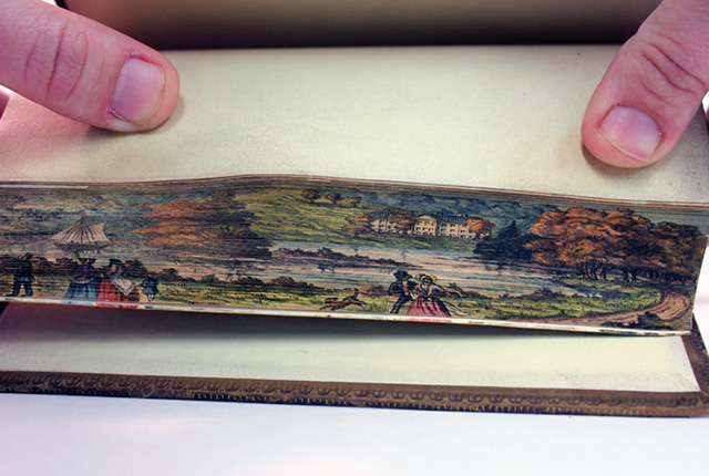 A fore-edge painting being positioned by hands