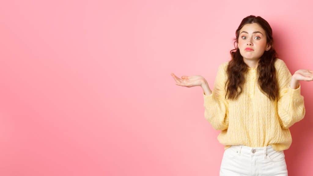 girl-in-yellow-sweater-shrugging-to-the-far-left-over-a-pink-background
