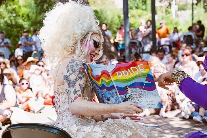Drag queen reading Pride book to children and families outdoors at a Drag Story Hour event