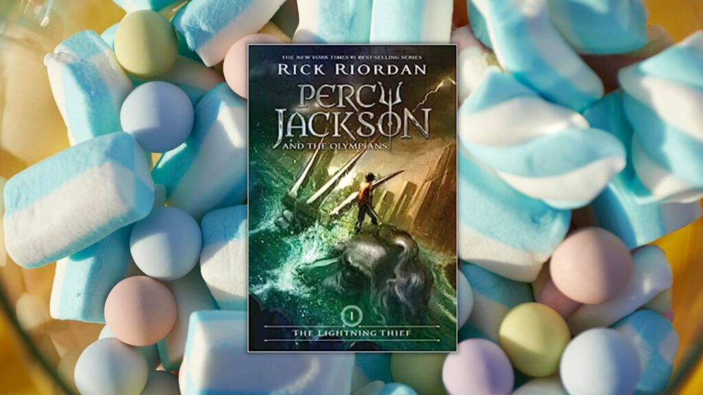 a-clear-bowl-of-blue-and-white-candy-with-pink-purple-and-yellow-candy-mixed-in. a-book-cover-is-on-top-with-a-picture-of-a-boy-standing-on-top-of-a-statue-percy-jackson-and-the-olympians-the-lightning-thief