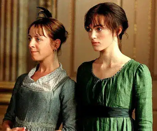 Elizabeth Bennet standing next to her friend Charlotte Lucas, both are wearing dresses and looking at a specific point in the room - Pride and Prejudice movie (year 2005)