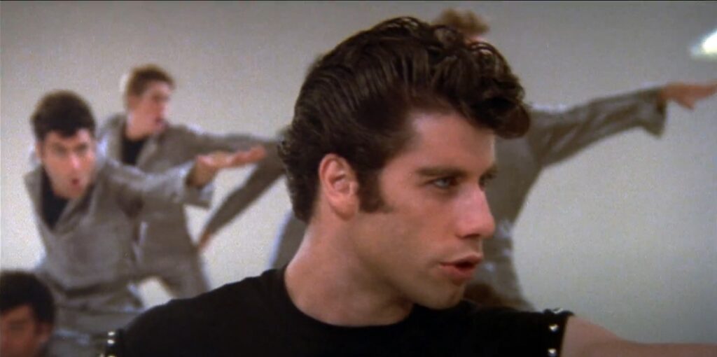 teenage-boy-wearing-black-tank-dancing-with-other-boys-in-background-grease