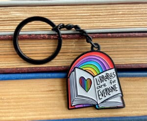 10-tempting-gifts-queer-book-nerds-will-love-libraries-are-for-everyone-book-with-rainbow-keychain-over-wood-background