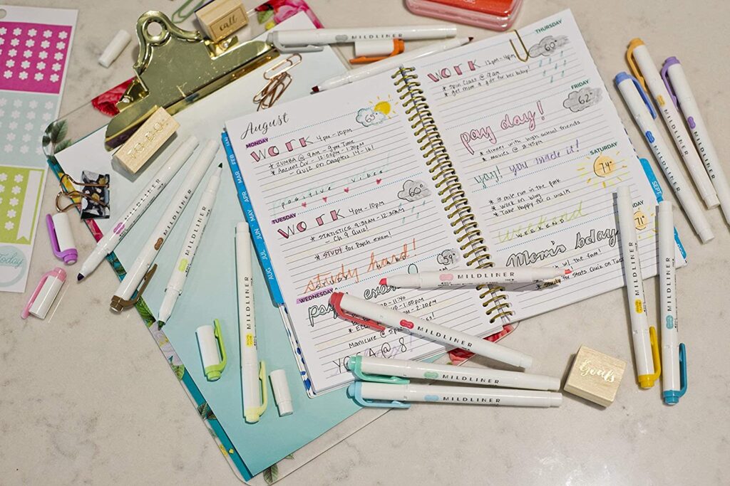 5-inexpensive-gifts-to-surprise-your-favorite-queer-writer-colorful-highlighters-scattered-around-a-used-open-notebook-and-a-clipboard