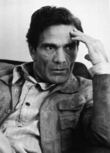 Black-and-white-photo-man-with-button-up-shirt-and-jacket-with-left-hand-up-to-his-forehead-looking-to-left-side