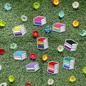 10-tempting-gifts-queer-book-nerds-will-love-nine-different-pride-flag-colored-books-on-a-grassy-background-with-flowers