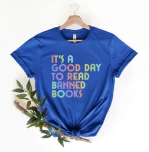 10-tempting-gifts-queer-book-nerds-will-love-blue-shirt-with-its-a-good-day-to-read-banned-books-written-in-rainbow-colors-on-a-hanger-near-a-branch