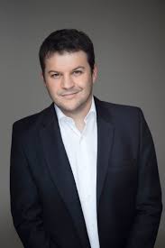 Guillaume Musso smiling with a gray background