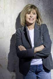 Katherine Pancol smiling with her arms crossed and a gray background