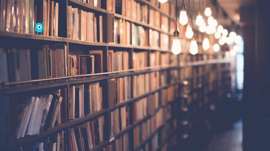 TBR-library-in-a-three-fourths-perspective-with-fairylights-hanging-in-the-middle-of-the-shelves-and-a-small-blue-monster-with-one-eye-on-one-of-the-shelves