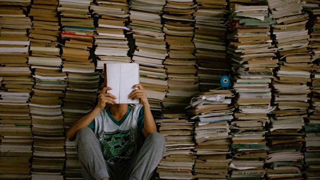person-reading-a-book-surrounded-by-their-to-be-read-pile-and-their-tbr-monster-is-next-to-them-in-the-dark-tbr