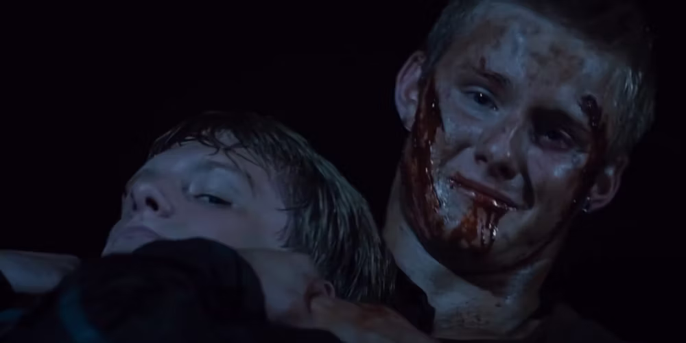 A man looking as if he's in pain, holding another man by the neck. His face is covered in blood.
